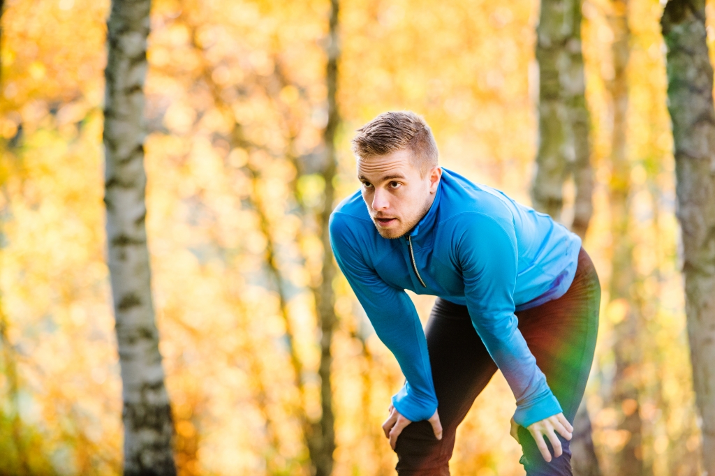 Young handsome hipster runner in blue sweatshirt outside in colorful sunny autumn nature