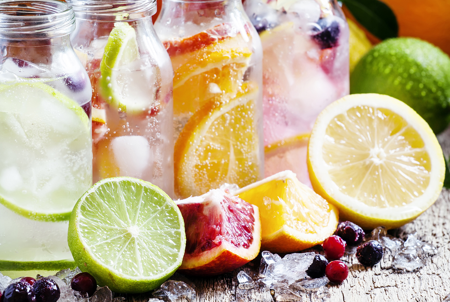 Fizzy water with citrus fruit, fresh berries and crushed ice, vintage wooden background, selective focus