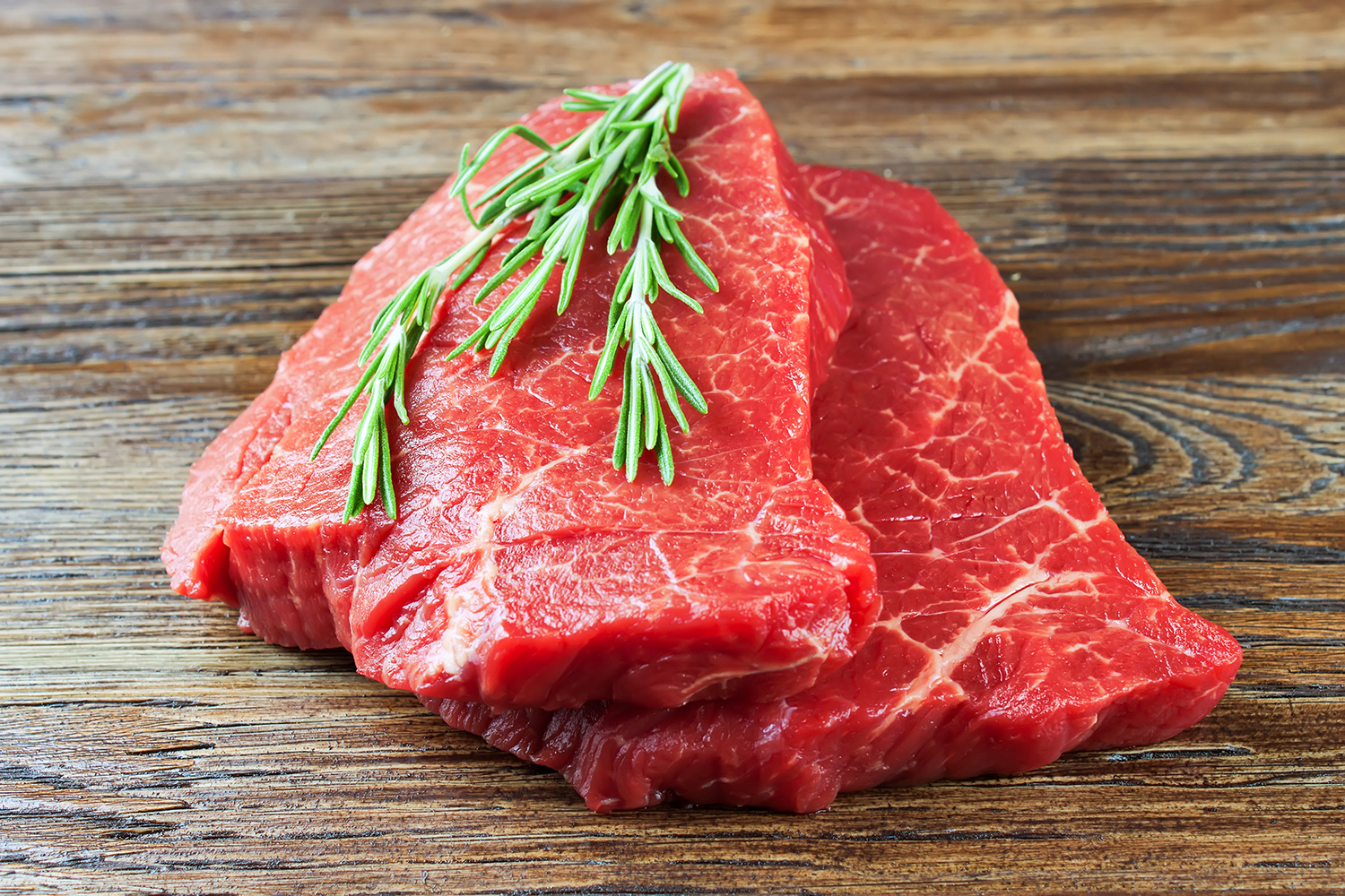 raw beef steak with rosemary on brown wooden background