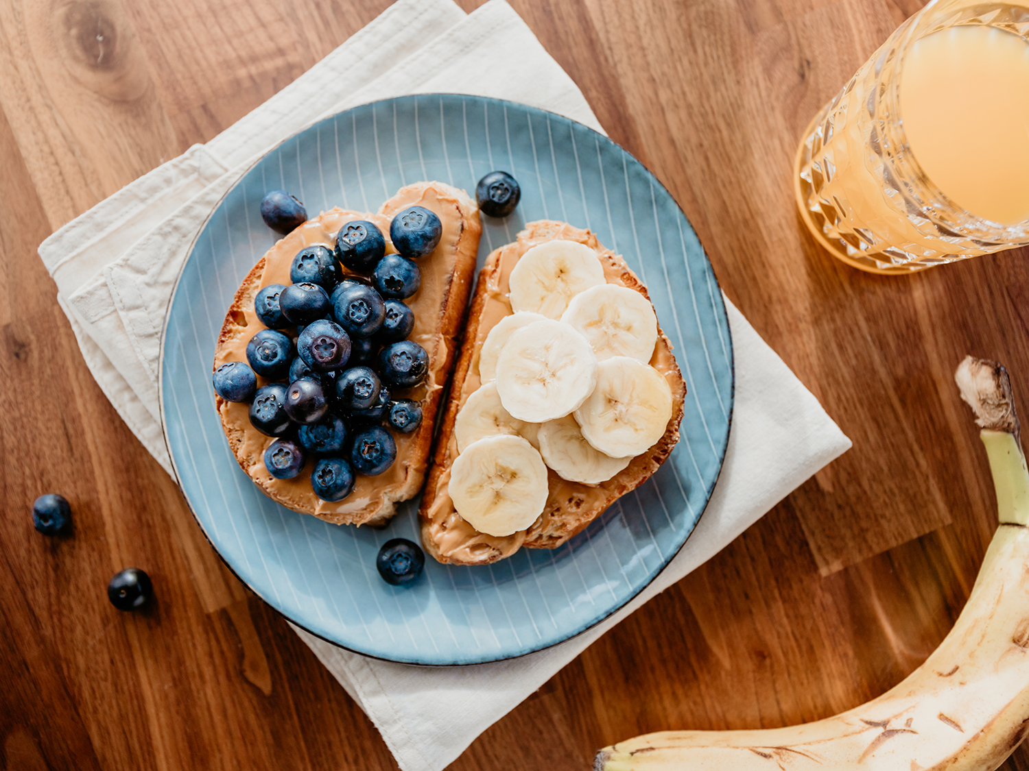 Two toasts with peanut butter, blueberry and banana. Healthy breakfast concept, top view.